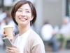 コーヒーとスマホをもって笑う女性