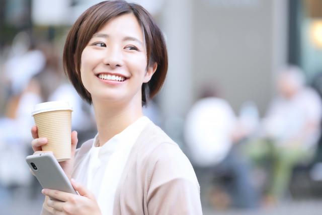 コーヒーとスマホをもって笑う女性