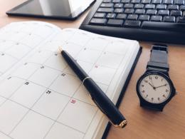 デスクの上の手帳、腕時計、ペン、パソコン