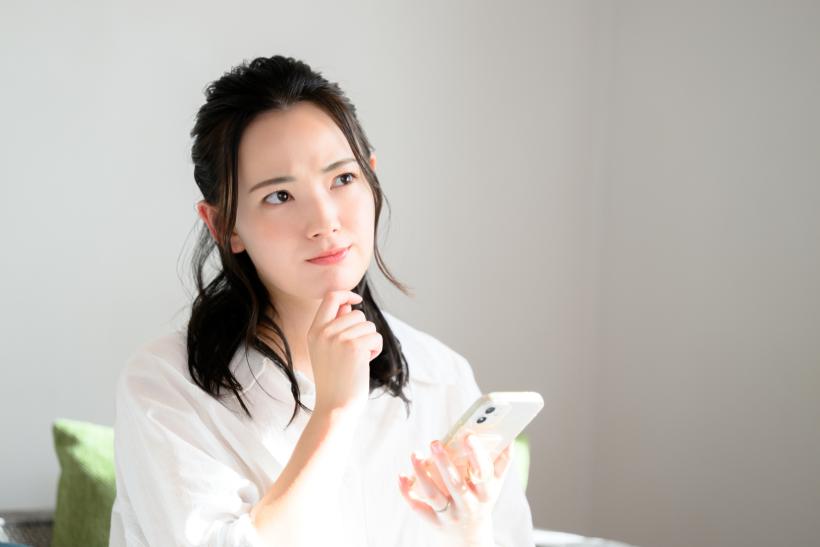 スマホを手に考える女性