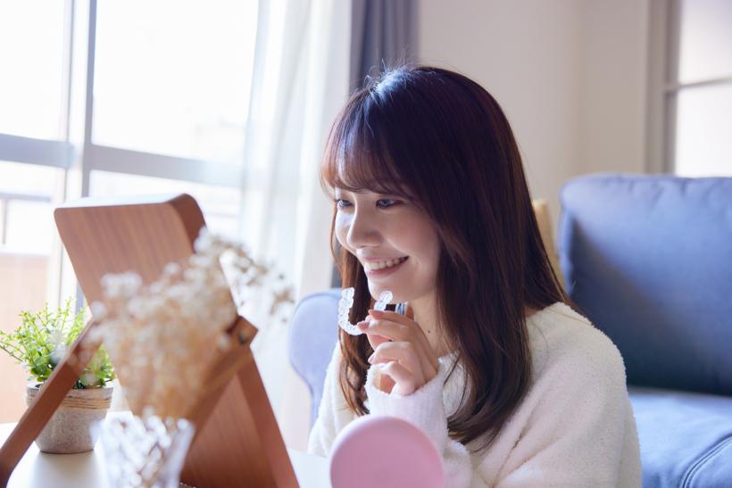 部屋でインビザラインを手に歯並びを確認する女性